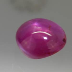 Könnte beinhalten: Ein rosa Edelstein im Cabochon-Schliff mit einer glatten, polierten Oberfläche.