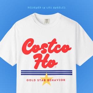 May include: White t-shirt with the words "Costco Ho" in red script, above blue stripes and a yellow star. The text "GOLD STAR BEHAVIOR" is below the stripes. The words "DESIGNED IN LOS ANGELES" are at the top.
