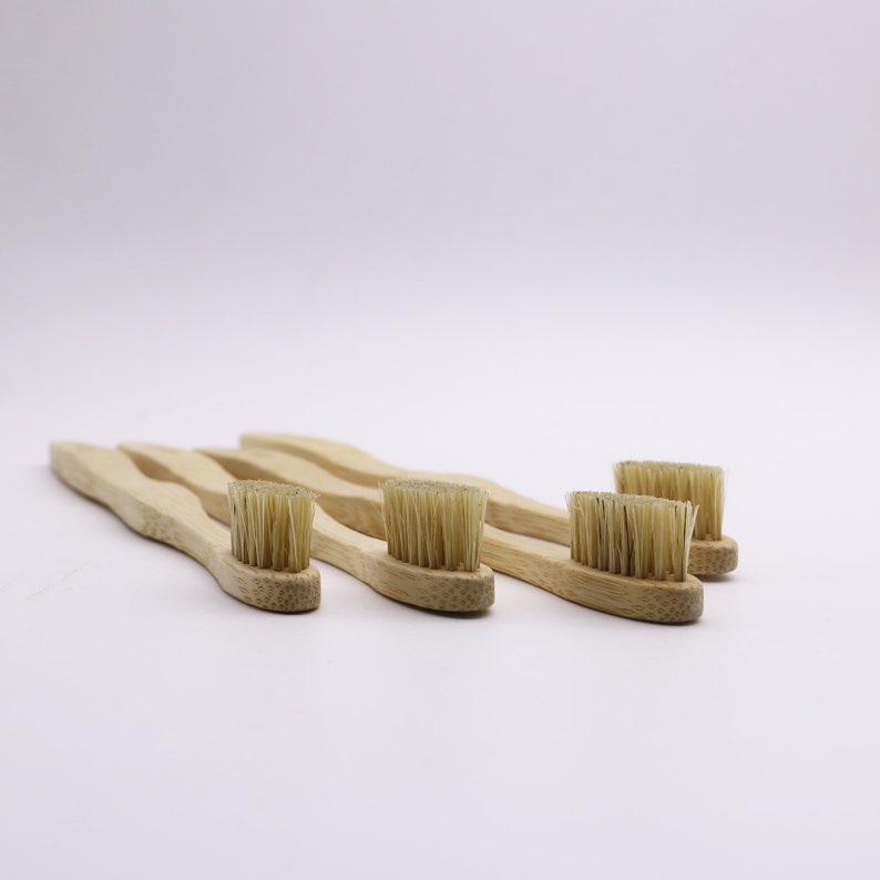 May include: Four natural bamboo toothbrushes with soft bristles. The toothbrushes are arranged in a row on a white surface.
