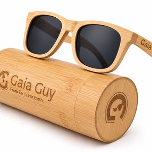 Könnte beinhalten: Sonnenbrille aus Holz mit dunklen Gläsern liegt auf einem passenden Bambus-Etui. Die Sonnenbrille hat einen quadratischen Rahmen und der Text "Gaia Guy" ist auf dem Bügel aufgedruckt. Das Etui trägt auch das "Gaia Guy"-Logo und den Text "From Earth. For Earth."
