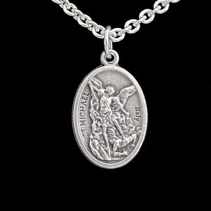 May include: A silver-toned oval pendant with an image of St. Michael, suspended from a matching chain. The pendant has the words "ST. MICHAEL" and "Italy" inscribed. The chain is a classic link style, and the background is black.