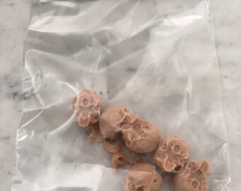 May include: A clear plastic bag containing several small, battle-damaged, tan-colored skull miniatures. The bag has a black and white label that reads "BAG of SKULLS" and "SMALL SKULLS (Battle Damaged)". The assembled size is 0.584"W x 0.713"D x 0.75"H.