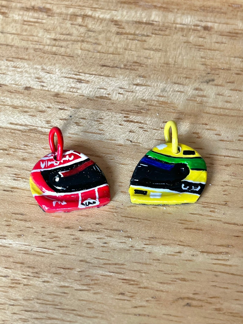 May include: Two small, painted helmet charms. One is red with black and white details, the other is yellow with green, blue, and black details.