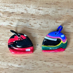 May include: Two small, hand-painted racing helmet charms. One is red with black and white stripes, the other is green, blue, and yellow with a white stripe.