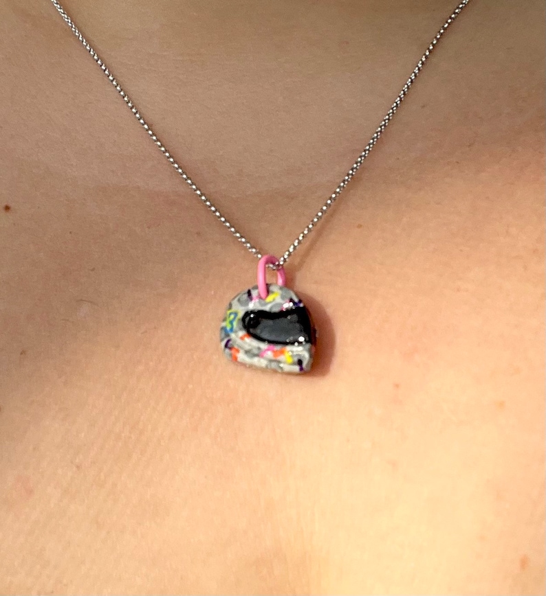 May include: A silver chain necklace with a small, colorful, helmet-shaped pendant. The helmet is white with black, yellow, blue, and pink accents.