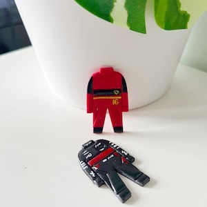 May include: Two toy racing suits, one red with a yellow stripe and the number 16, and one black with red and white stripes.