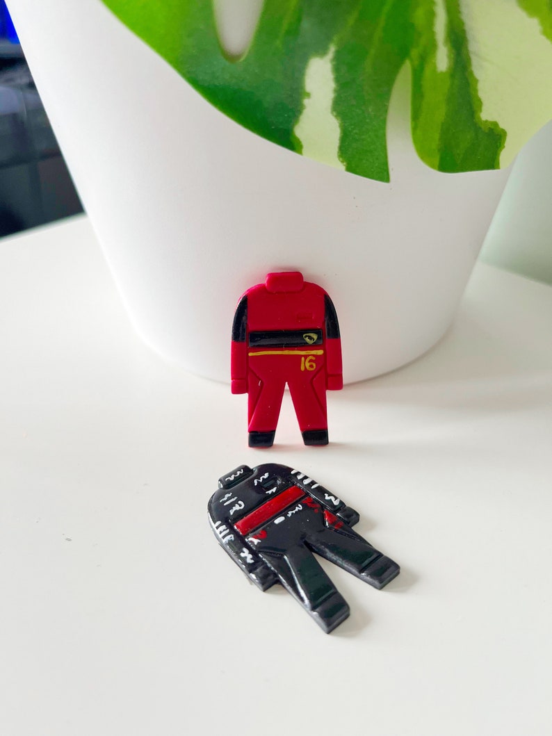 May include: Two toy racing suits, one red with a yellow stripe and the number 16, and one black with red and white stripes.