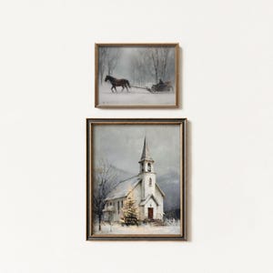 May include: Two framed winter landscape paintings. The top painting depicts a horse-drawn sleigh in a snowy forest. The bottom painting shows a white church with a steeple, a Christmas tree, and snow-covered ground. Both paintings have gold frames.