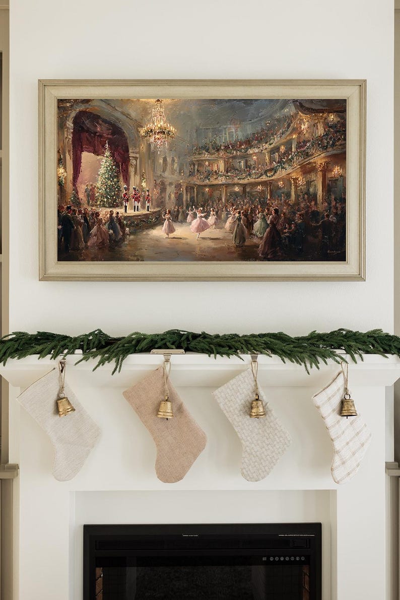 May include: A framed painting of a festive ball scene hangs above a fireplace. Below, four Christmas stockings in neutral tones are suspended from the mantel, each adorned with a small gold bell and a garland of greenery.