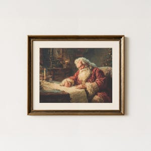 May include: A framed print depicts Santa Claus writing at a desk. He wears a red coat with white fur trim and has a long white beard. The print has a gold-colored frame and is set against a white wall. A candle and other objects are on the desk.