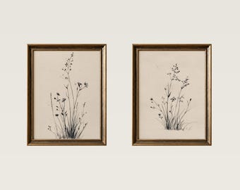 May include: Two framed botanical prints. Each print features a detailed pen and ink drawing of wildflowers and grasses. The artwork is set against a cream-colored background and framed in a gold-toned frame. The overall aesthetic is vintage and natural.