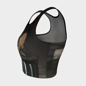 May include: A black and brown crop top with a graphic print of a person sitting on a trash can. The top has a racerback style and a cropped length.