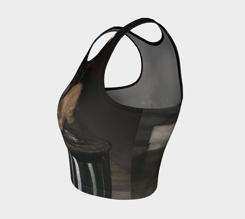 May include: A black and brown crop top with a graphic print of a person sitting on a trash can. The top has a racerback style and a cropped length.