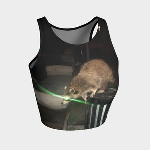 May include: A black tank top with a graphic print of a raccoon looking at a green laser light. The raccoon is standing on a black and white striped trash can.