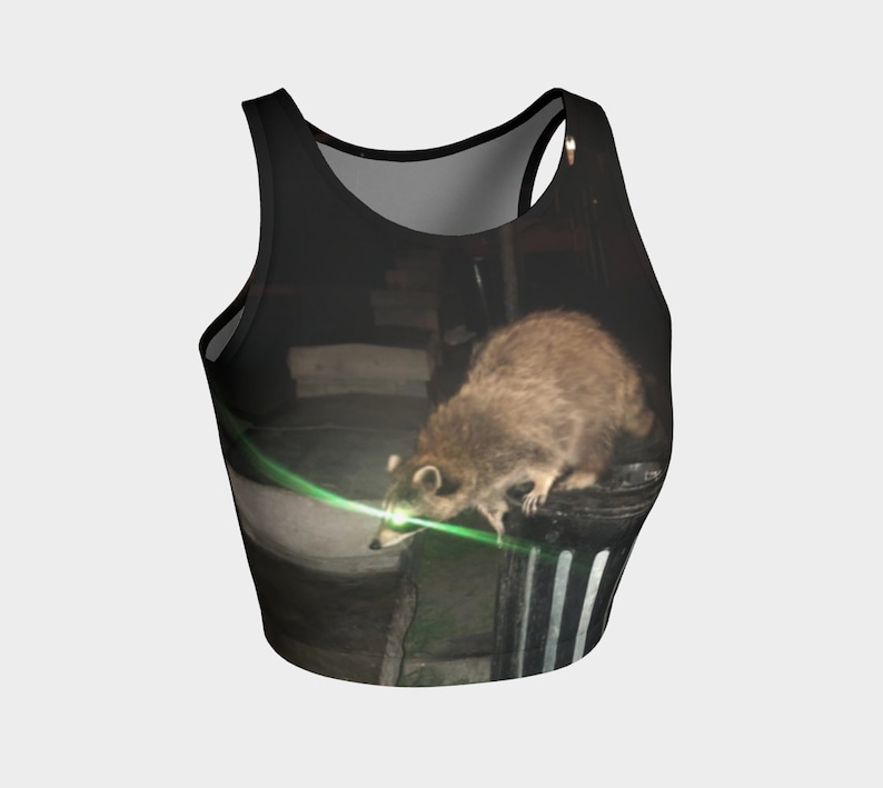 May include: A black tank top with a graphic print of a raccoon looking at a green laser light. The raccoon is standing on a black and white striped trash can.