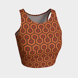 May include: A sleeveless crop top with a geometric pattern in shades of orange and brown. The pattern resembles a maze or a honeycomb.
