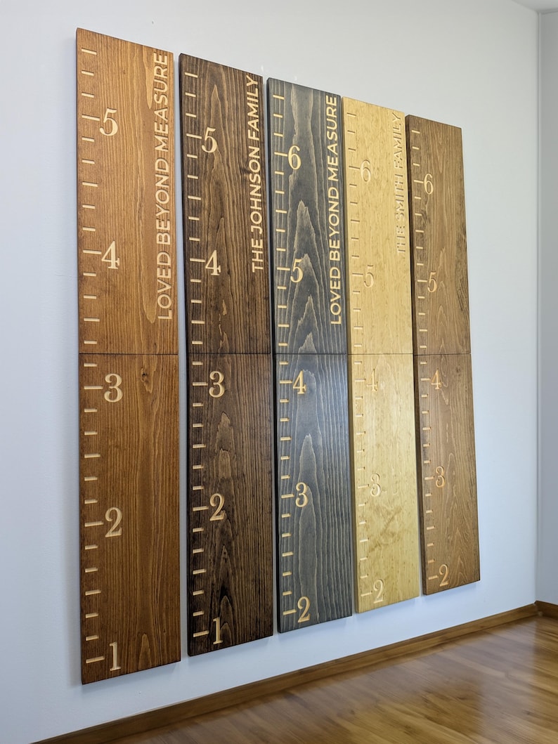 May include: A set of wooden height charts in shades of brown, featuring engraved markings and numbers. The text "LOVED BEYOND MEASURE" and family names are also engraved. These decorative charts are designed to track a child's height.