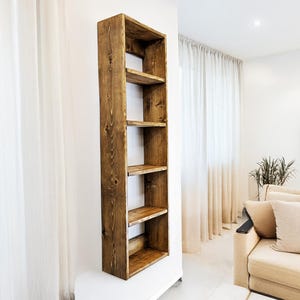 May include: A tall, rustic wooden bookshelf with five shelves. The bookshelf is made of stained wood and is mounted on a white wall. The shelves are open and ready for display. The style is modern farmhouse.