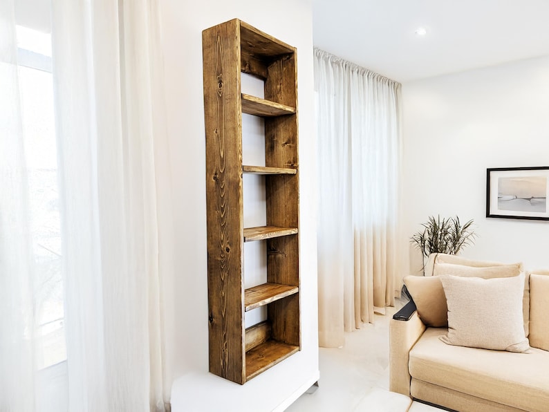 May include: A tall, rustic wooden bookshelf with five shelves. The bookshelf is made of stained wood and is mounted on a white wall. The shelves are open and ready for display. The style is modern farmhouse.