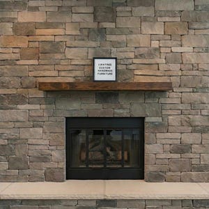 May include: A fireplace set into a stone wall, featuring a dark wooden mantel and a black firebox. Above the mantel is a sign that reads "IRNTREE CUSTOM HANDMADE FURNITURE."