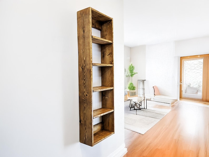 May include: A tall, rectangular wooden shelf with five open shelves, mounted on a white wall. The shelf is made of stained wood, showcasing the natural grain and knots. The shelves are evenly spaced, offering storage or display space.