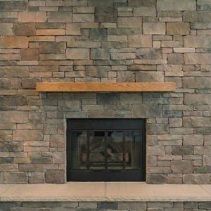 May include: A stone fireplace with a wooden mantel. The stone is a mix of grey, brown, and tan rectangular blocks. The fireplace opening is black with glass doors, and a stone hearth is at the base.