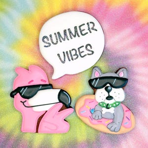 Puede incluir: Galletas con forma de flamenco rosa y bulldog gris con gafas de sol, con un bocadillo blanco que dice "SUMMER VIBES" en letras brillantes. El bulldog flota en una rosquilla.