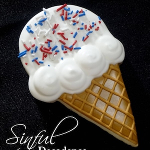 Könnte beinhalten: Ein Keks in Form einer Eistüte, verziert mit weißem Zuckerguss und roten, weißen und blauen Streuseln. Die Tüte ist hellbraun mit einem Waffelmuster. Die Worte "Sinful Decadence" sind in einer Schreibschrift geschrieben.