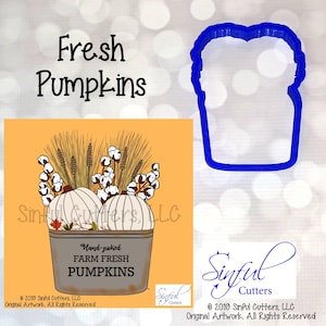 May include: A blue plastic cookie cutter in the shape of a loaf of bread sits next to a fall-themed illustration. The illustration features two pumpkins in a metal container with wheat, cotton, and the text "Fresh Pumpkins".