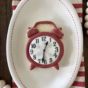 May include: A red and white alarm clock cookie decorated with a snowflake on a white plate with a red and white striped tablecloth.