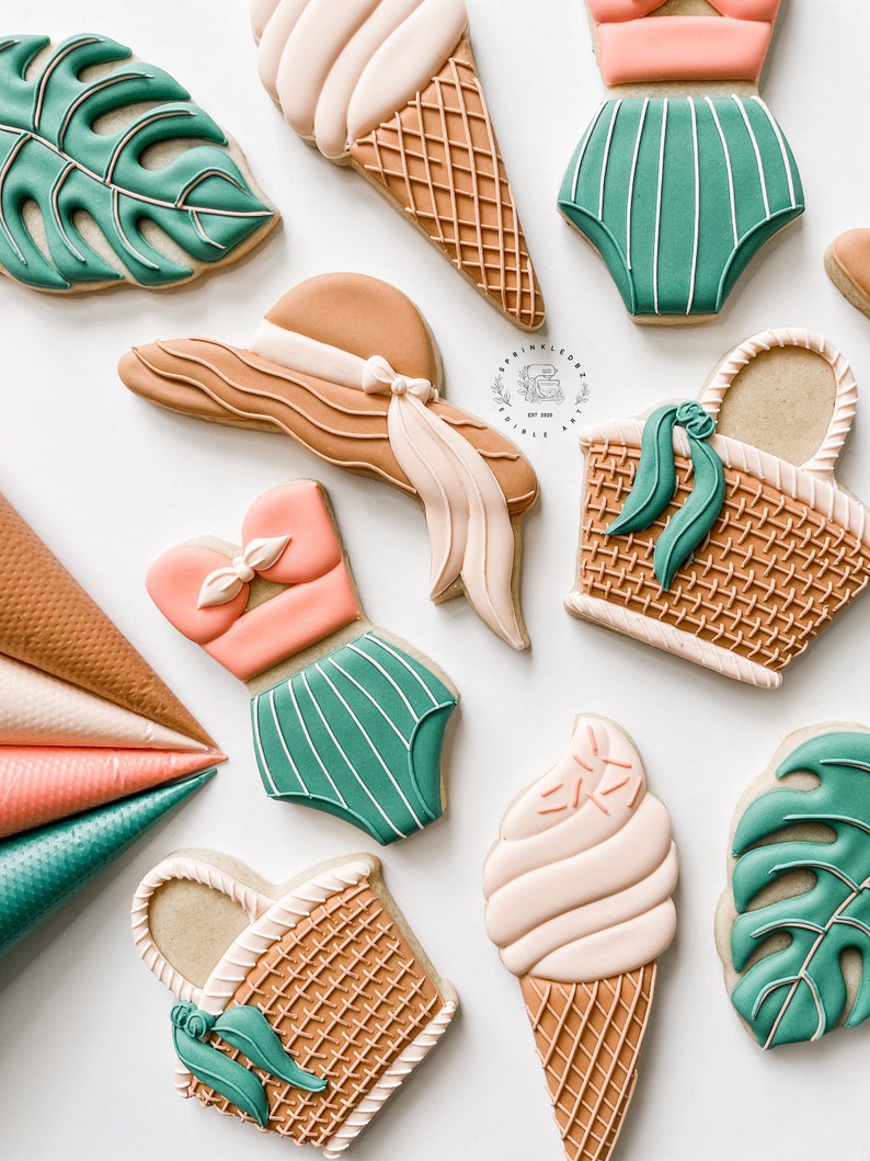 May include: A set of nine decorated sugar cookies featuring summer themes. The cookies are decorated with various colors, including brown, green, pink, and white. The cookies depict a beach hat, a swimsuit, a basket, an ice cream cone, and tropical leaves.