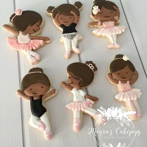 Op de afbeelding: Versierde suikerkoekjes in de vorm van ballerina's. Elk koekje toont een bruinharige ballerina in een roze tutu en balletschoenen. Sommige ballerina's dragen zwarte turnpakjes. De koekjes zijn gerangschikt op een wit oppervlak.