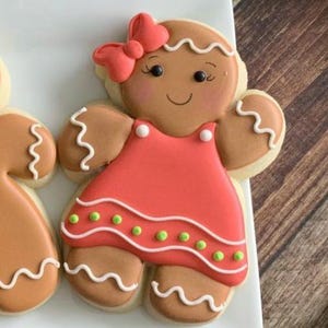 May include: Gingerbread cookie decorated with red and white icing. The cookie is shaped like a person wearing a red dress with white and green accents.