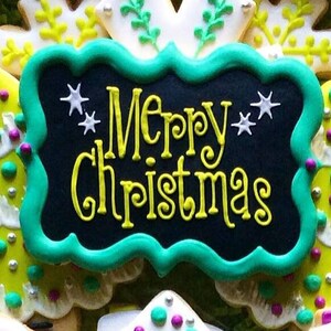 May include: A decorated cookie with a black background and the words "Merry Christmas" in yellow script. The cookie is framed with a green border and decorated with white star accents. Other cookies are visible in the background.