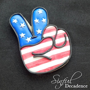 May include: A peace sign cookie decorated with red, white, and blue icing to resemble the American flag.