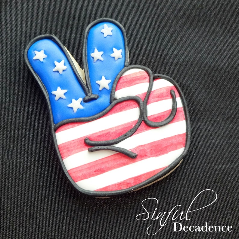 May include: A peace sign cookie decorated with red, white, and blue icing to resemble the American flag.