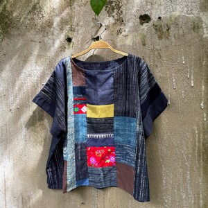 May include: A short-sleeved top constructed from various fabric patches in shades of blue, brown, yellow, and red. The garment features a mix of solid colours, striped textures, and a floral print panel, all assembled into a patchwork design.