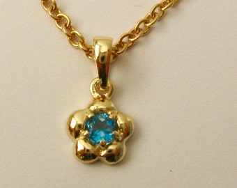 Pode incluir: Um colar de corrente de ouro com um pequeno pingente de flor com uma pedra preciosa azul.