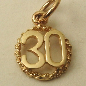 Peut inclure: Un pendentif en forme de breloque de couleur or, représentant le chiffre "30" à l'intérieur d'un cadre circulaire texturé. Le pendentif est doté d'une boucle en haut pour l'attacher à un collier ou un bracelet. La breloque est probablement en or ou en métal doré.