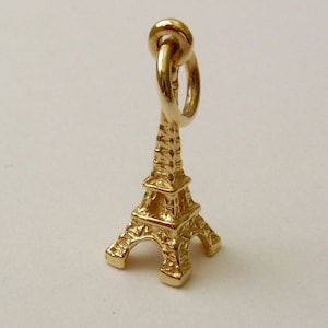 May include: A gold-coloured Eiffel Tower charm, with detailed architectural features. The charm has a loop at the top for attaching to a necklace or bracelet. The iconic structure is a symbol of Paris and French culture.
