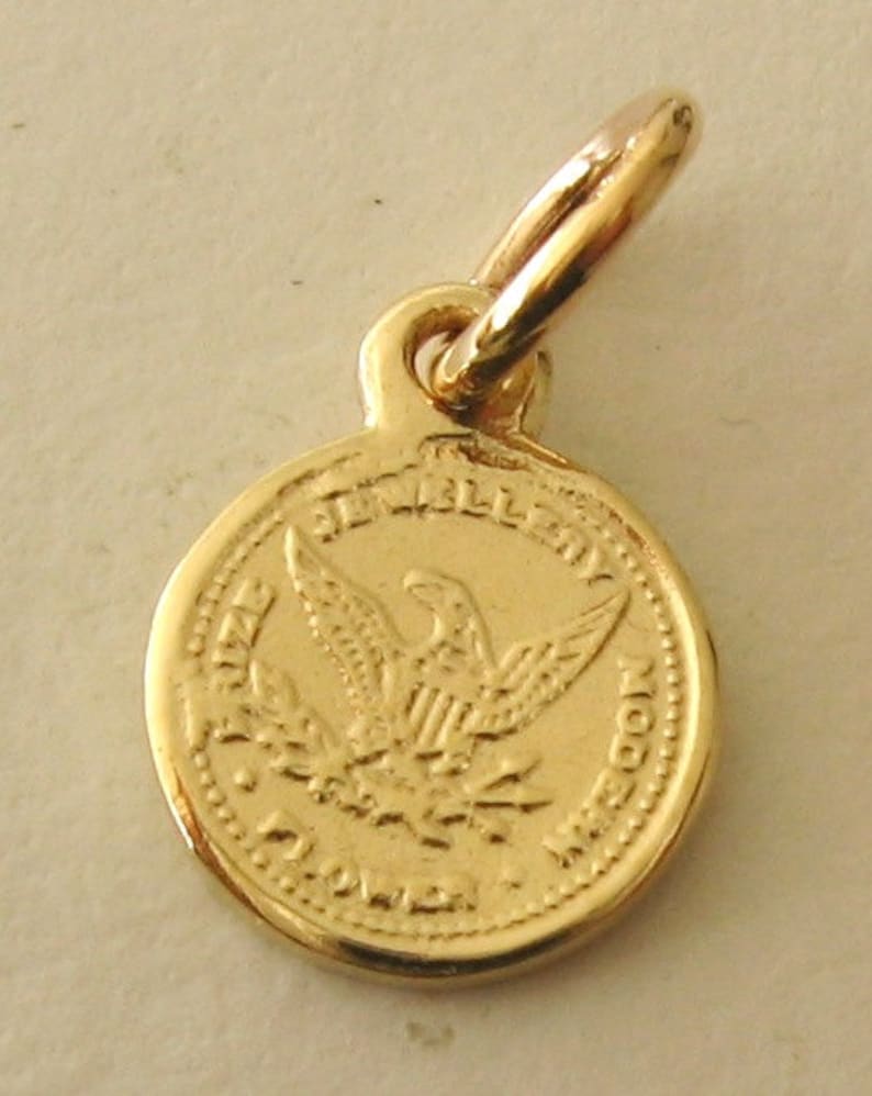 May include: Gold-toned charm featuring an eagle with outstretched wings and the words "The United States of America" around the edge.