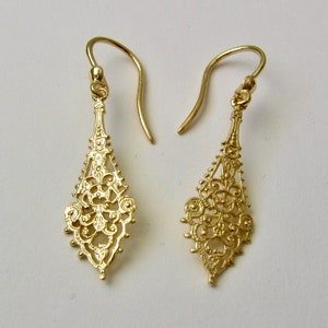 May include: A pair of gold filigree dangle earrings with a delicate, intricate design. The earrings are made of a thin, lightweight metal and have a drop shape.
