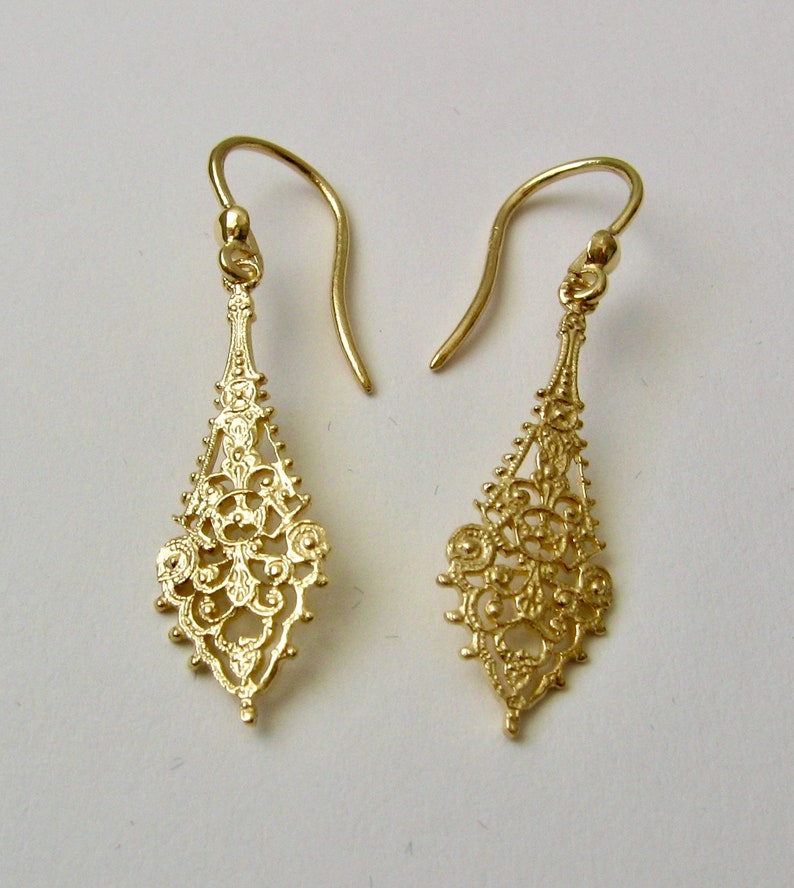 May include: A pair of gold filigree dangle earrings with a delicate, intricate design. The earrings are made of a thin, lightweight metal and have a drop shape.