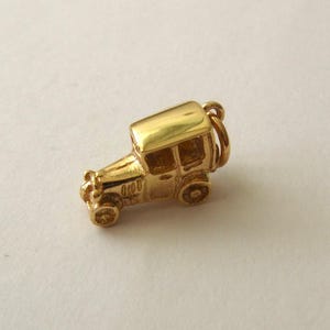 May include: A gold-coloured charm in the shape of a vintage car. The charm features a detailed design of a classic automobile with a roof, windows, and wheels. The charm has a loop for attaching to a bracelet or necklace.