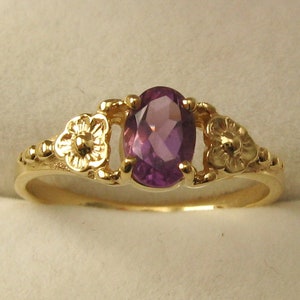 May include: A gold ring featuring a purple oval gemstone set within two floral designs.