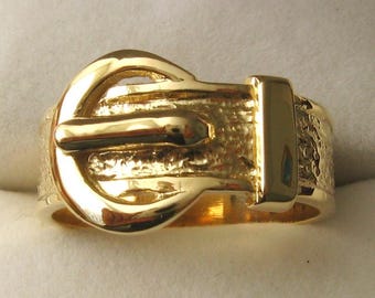 May include: A gold-colored ring shaped like a belt buckle. The buckle is textured and has a shiny finish.