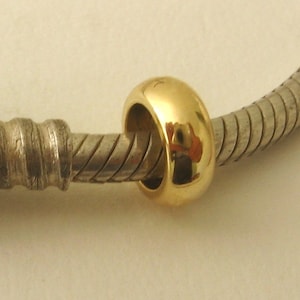 Peut inclure: Un charme en forme d'anneau de couleur dorée, attaché à un bracelet en argent.