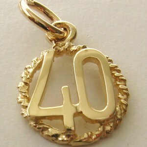 May include: Gold charm with the number 40 in a rope-like circle. The charm is a pendant for a necklace or bracelet.