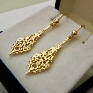May include: A pair of gold filigree dangle earrings with a delicate, intricate design. The earrings are made of a thin, lightweight metal and have a drop shape.
