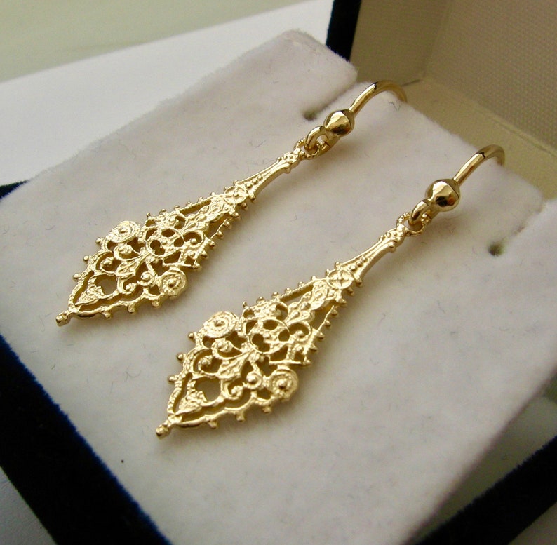 May include: A pair of gold filigree dangle earrings with a delicate, intricate design. The earrings are made of a thin, lightweight metal and have a drop shape.